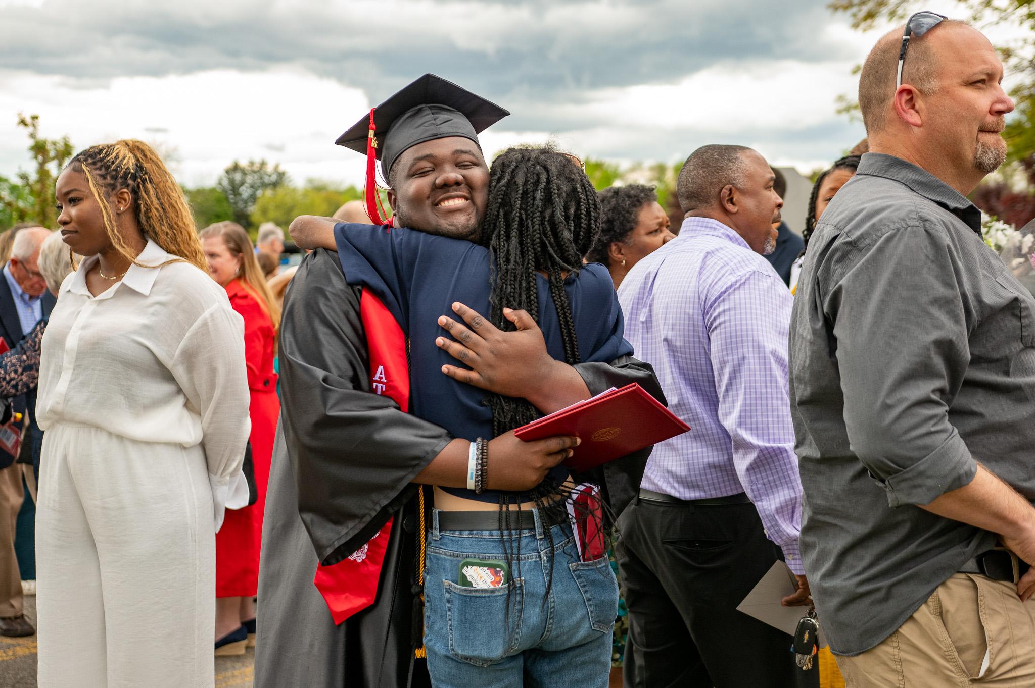 A graduate in a cap and gown hugs a loved one at Roberts Wesleyan University's commencement ceremony